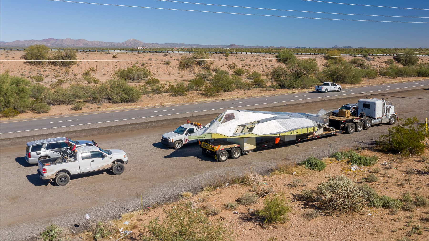Chrome tractor hauling heavy equipment on a double-drop lowboy trailer staged in a yard.