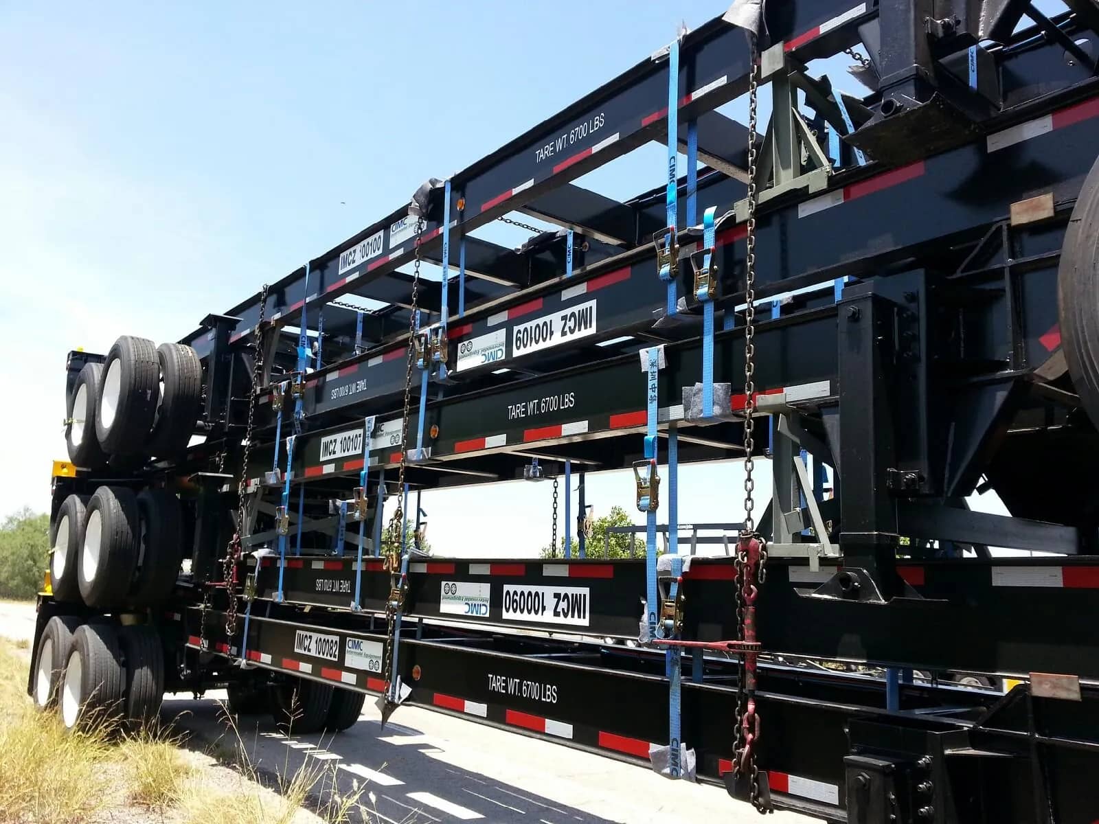 Step deck trailer with secured machinery ready for transport in a yard.