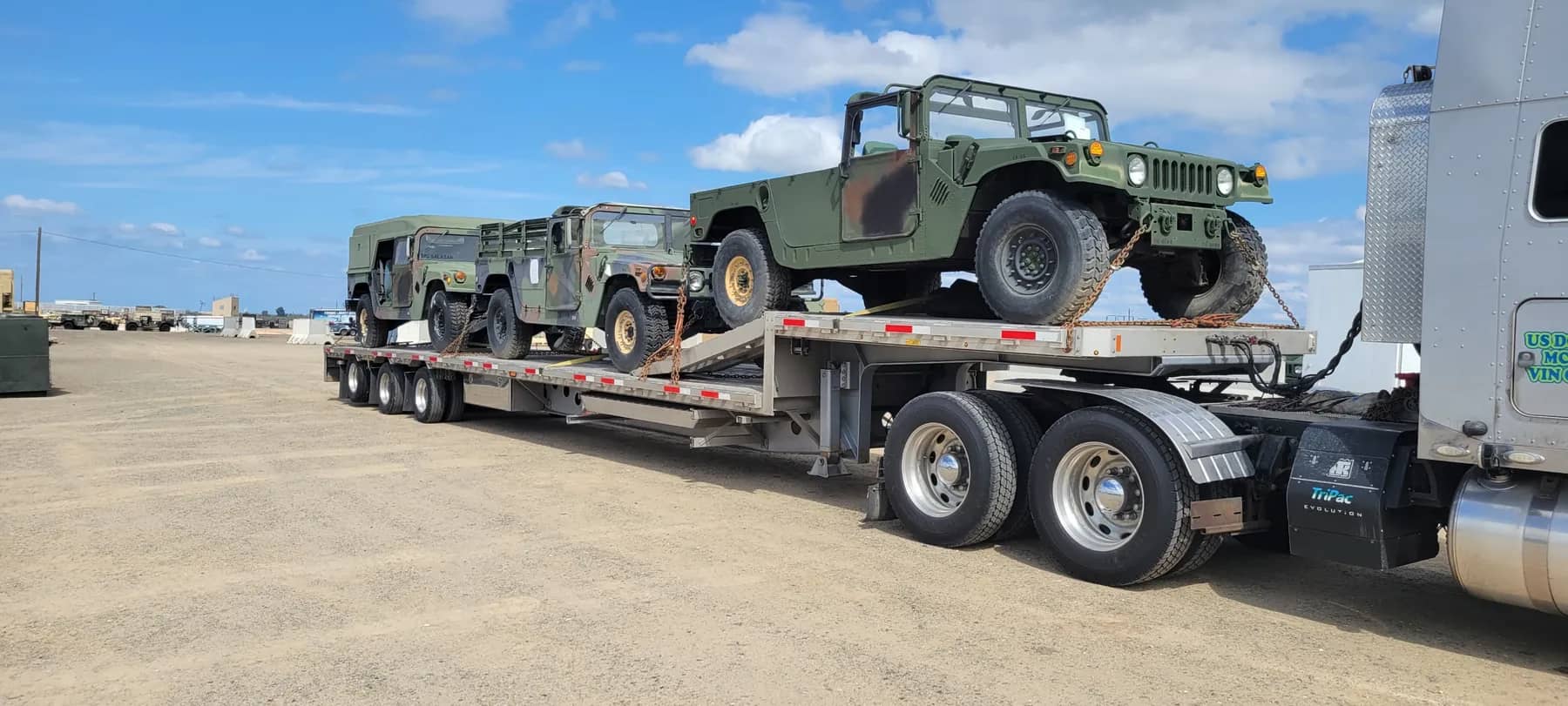 Step deck trailer with heavy equipment secured in a yard before dispatch.