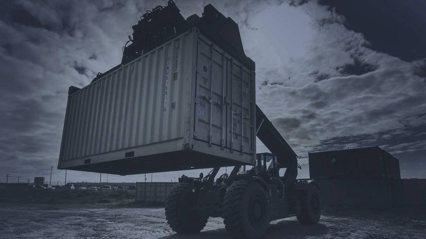 Container handler lifting a container in a port yard.