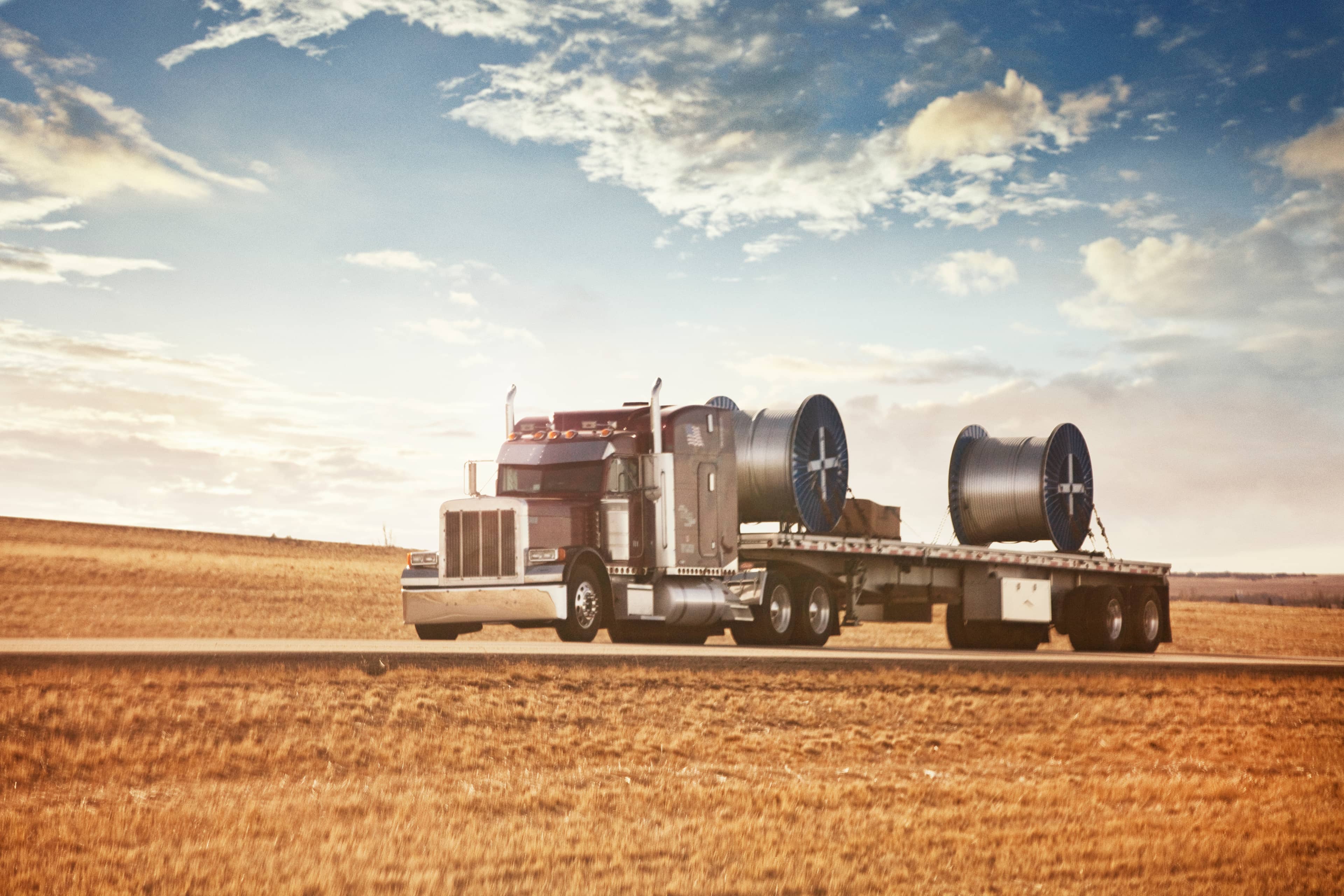 Steel coils secured on a flatbed trailer with chains and coil racks.