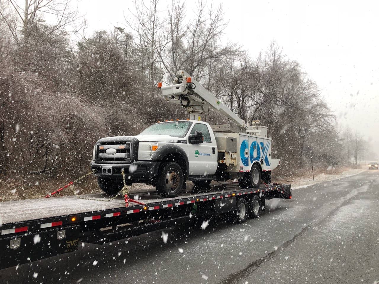 Bucket truck on a gooseneck hotshot trailer during snowfall.