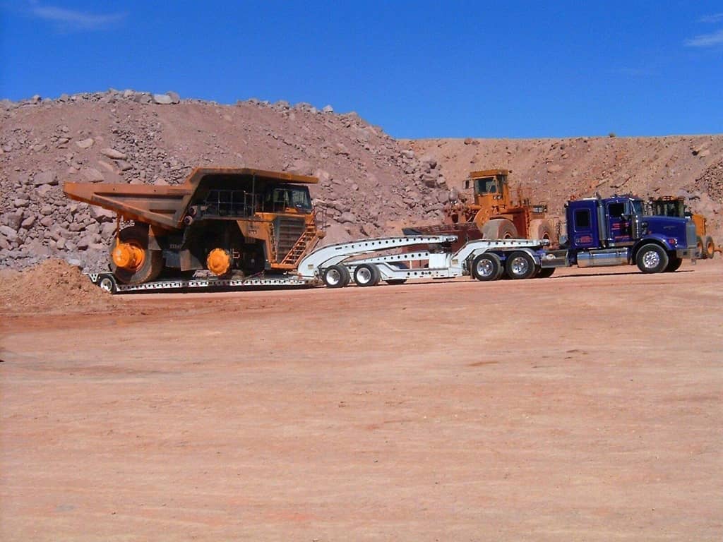 Multi-axle trailer hauling a 777 rigid-frame truck coming out of a quarry.